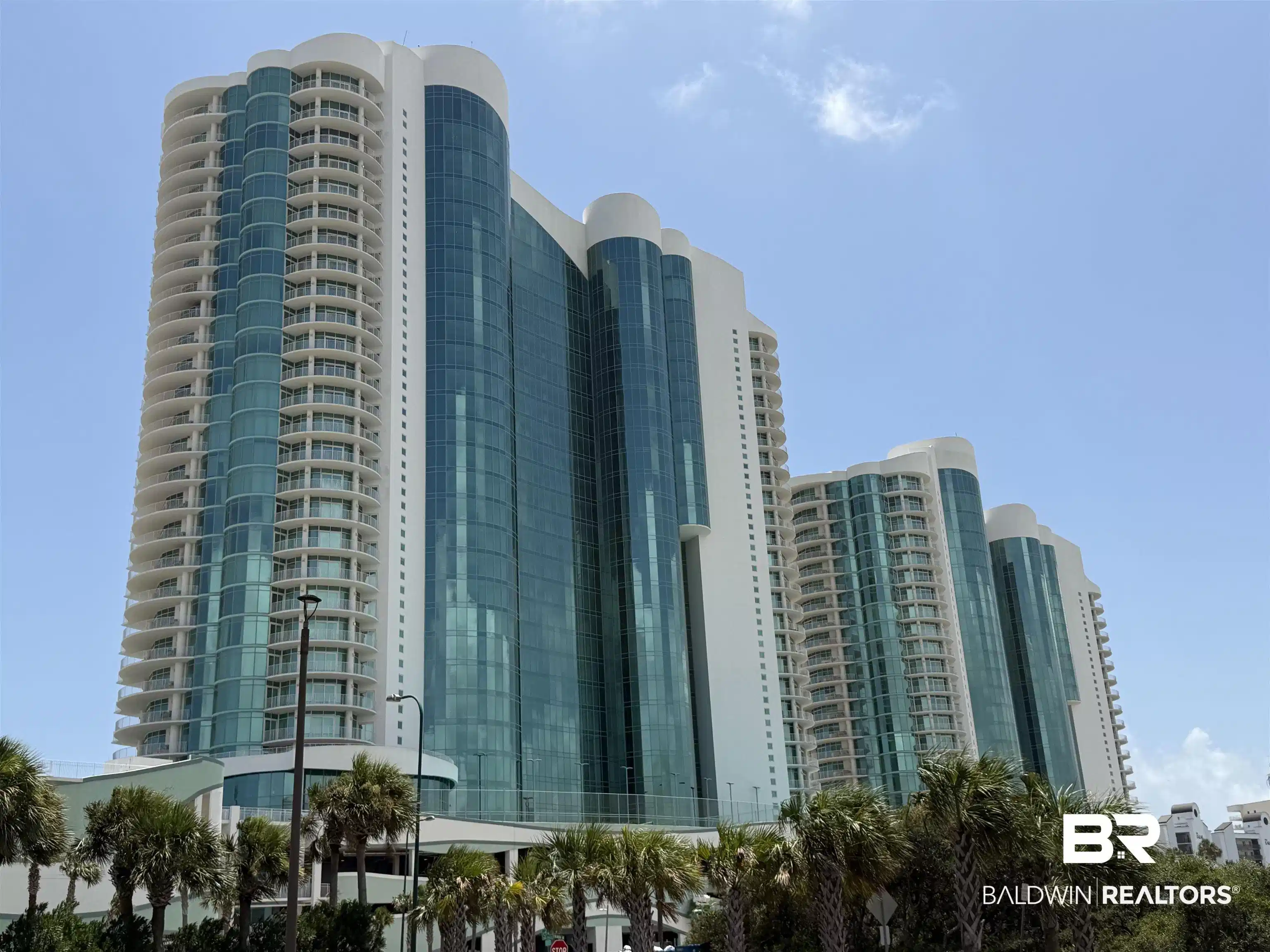 Image 1: Modern high-rise residential building featuring a distinctive curved facade, extensive glass curtain walls, numerous private balconies, and a white architectural finish