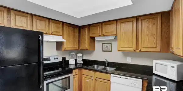 Image 2: Kitchen with white appliances, light tile patterned floors, a sink, under cabinet range hood, and brown cabinets