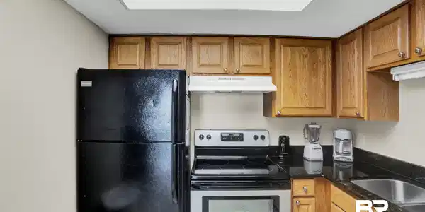 Image 3: Kitchen featuring under cabinet range hood, dark stone countertops, stainless steel range with electric cooktop, brown cabinets, and freestanding refrigerator