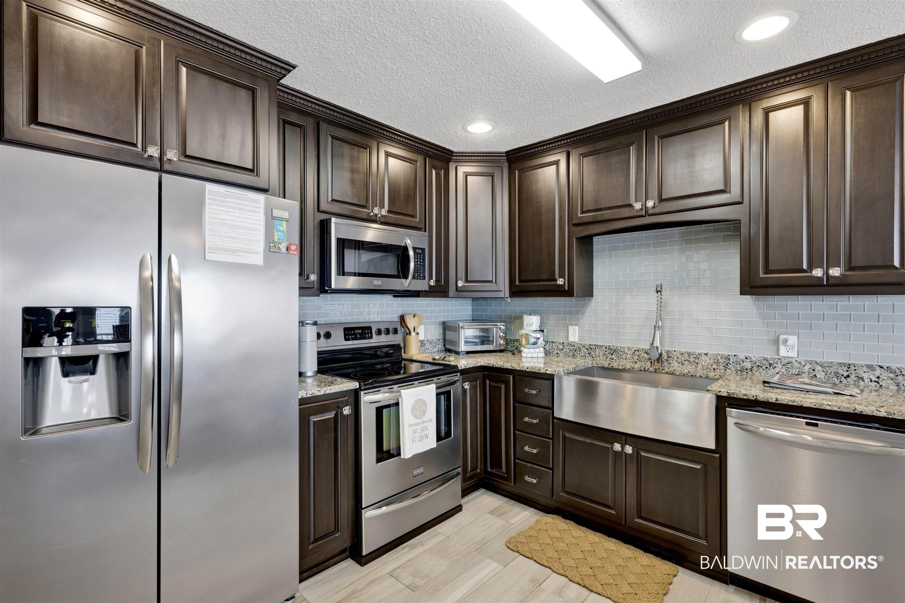 Image 4: Kitchen with stainless steel appliances, dark wood finish cabinets, light stone countertops, recessed lighting, and a textured ceiling