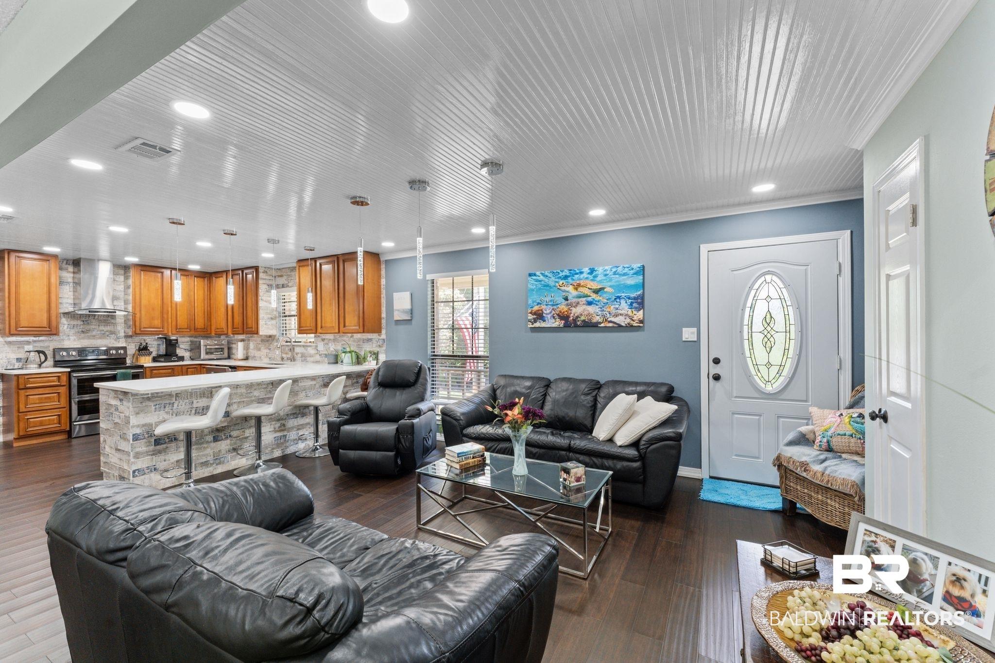 Image 4: Open-concept living space featuring wood-finish flooring, a beadboard ceiling with recessed lighting, and a kitchen island with a stone facade and pendant lighting