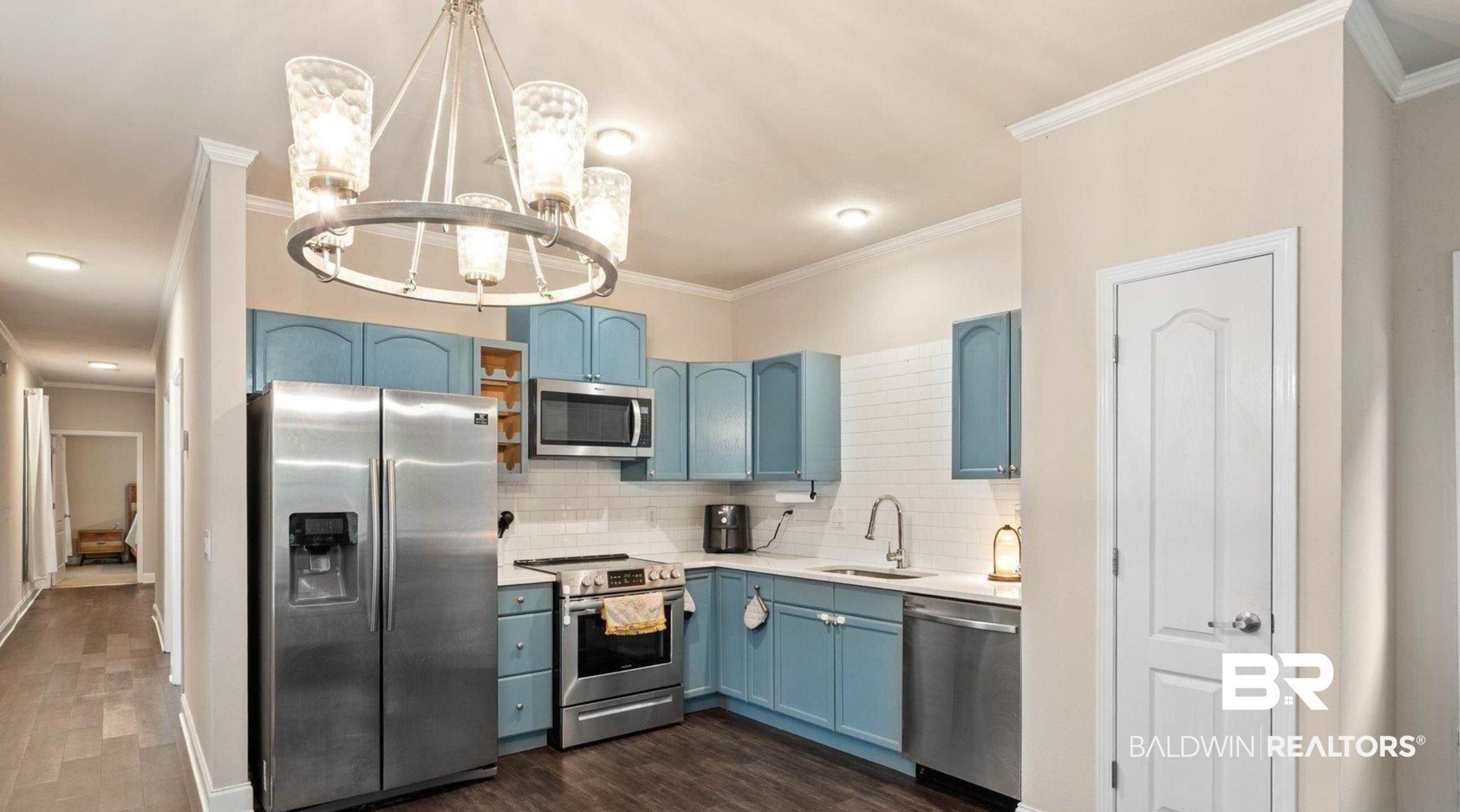 Image 4: Kitchen with blue cabinetry, appliances with stainless steel finishes, backsplash, crown molding, and hanging light fixtures