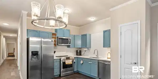 Image 4: Kitchen with blue cabinetry, appliances with stainless steel finishes, backsplash, crown molding, and hanging light fixtures