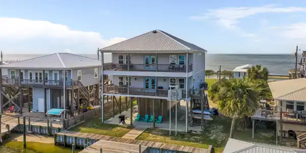 Image 2: Elevated coastal residence featuring a metal roof, multiple covered balconies, a private boat dock, and direct water frontage