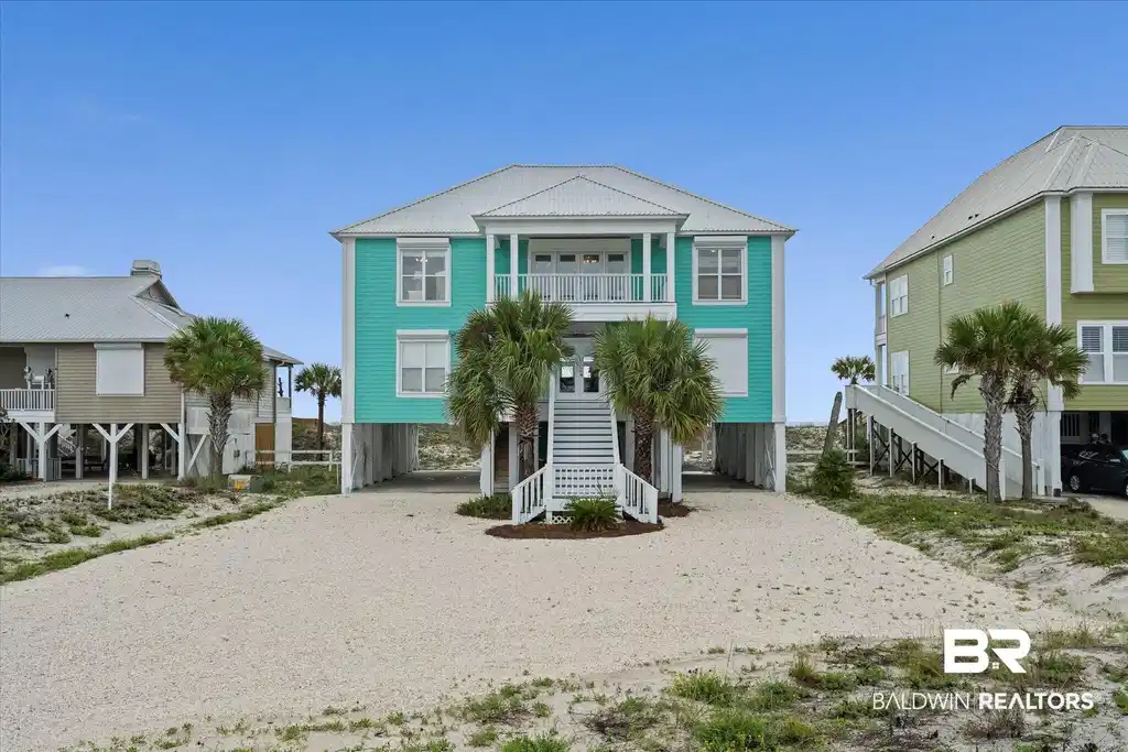 Image 1: Elevated coastal home featuring a turquoise exterior, white trim, and a metal roof