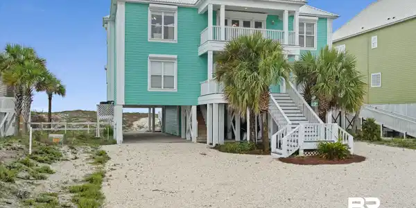 Image 2: Stilted coastal residence featuring a teal exterior, white metal roof, and a gravel driveway