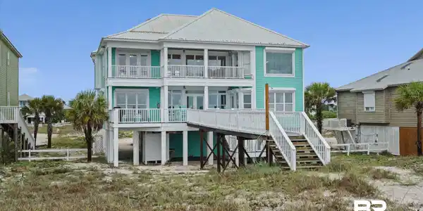 Image 3: Multi-story coastal residence featuring a vibrant teal exterior, white trim, and a metal roof