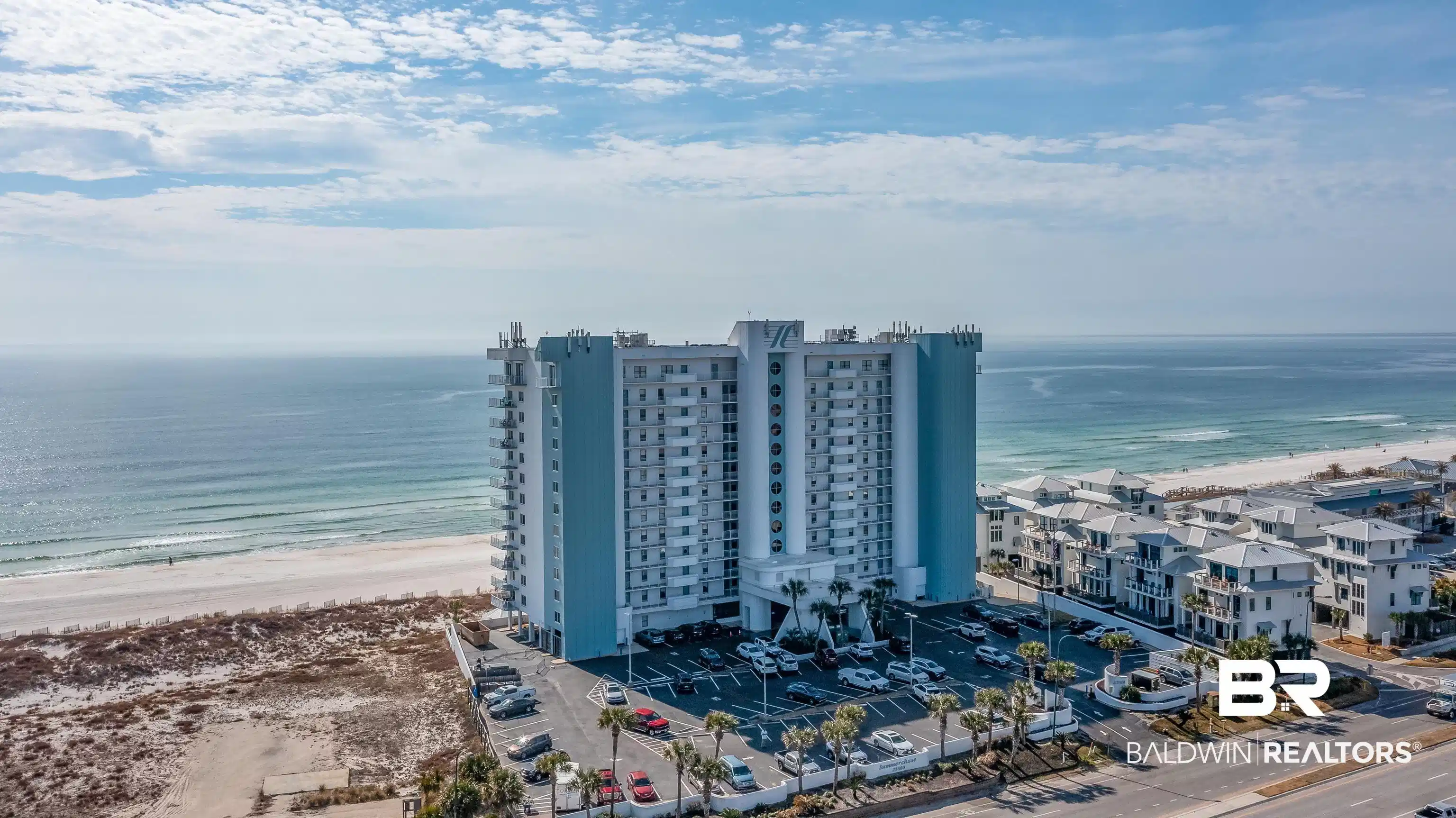 Image 1: Multistory building with light blue and white exterior, featuring a beachfront location directly on a sandy shore