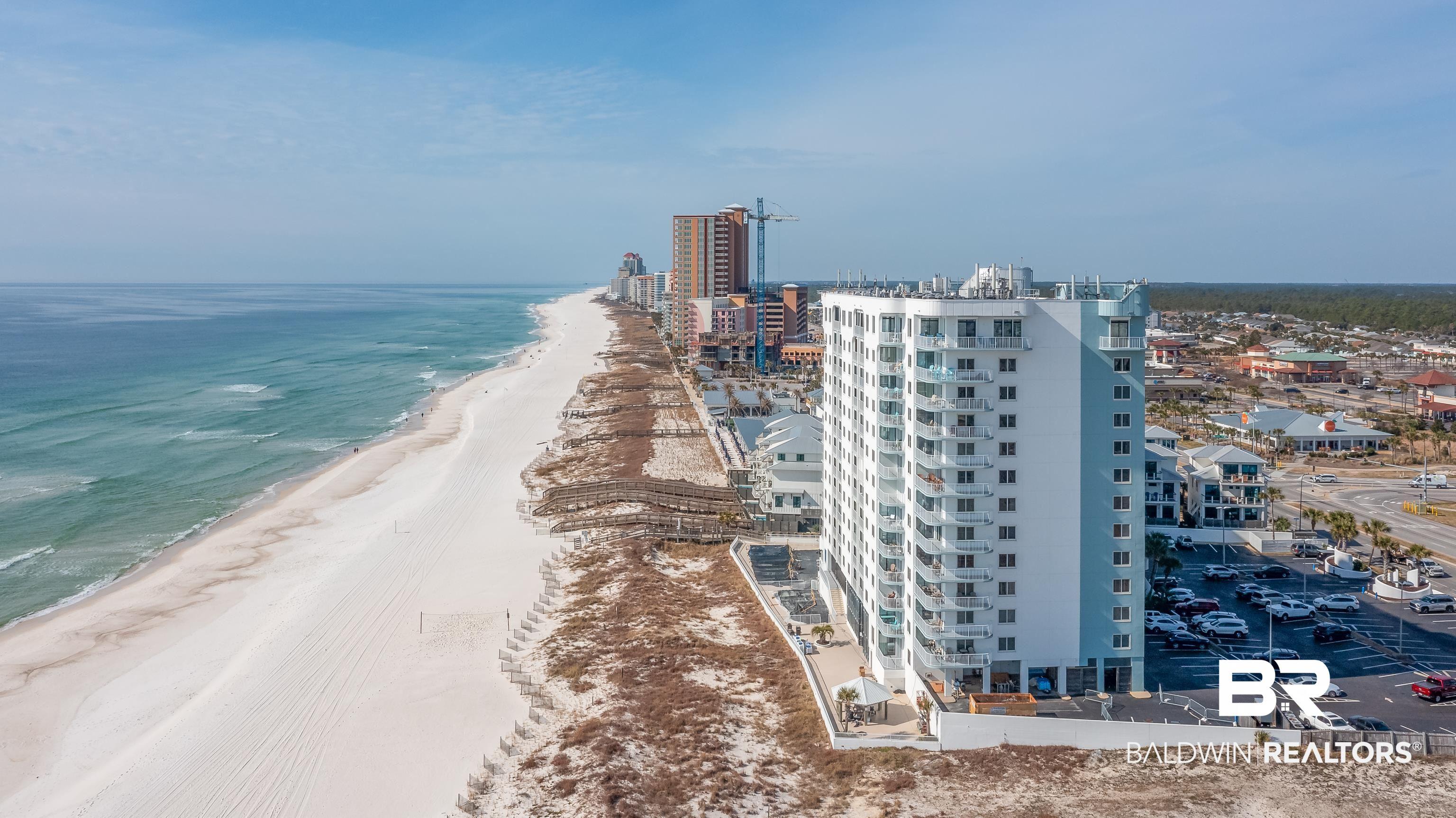 Image 2: Modern multi-story building featuring individual balconies, a light-colored facade, and proximity to a wide sandy beach with clear blue waters