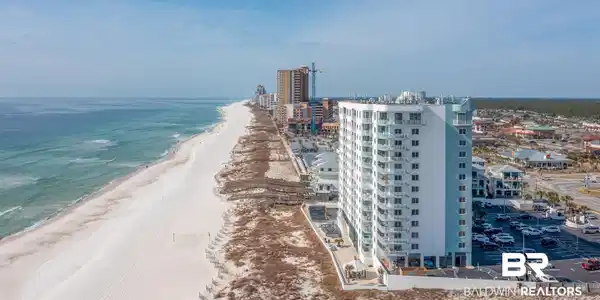 Image 2: Modern multi-story building featuring individual balconies, a light-colored facade, and proximity to a wide sandy beach with clear blue waters