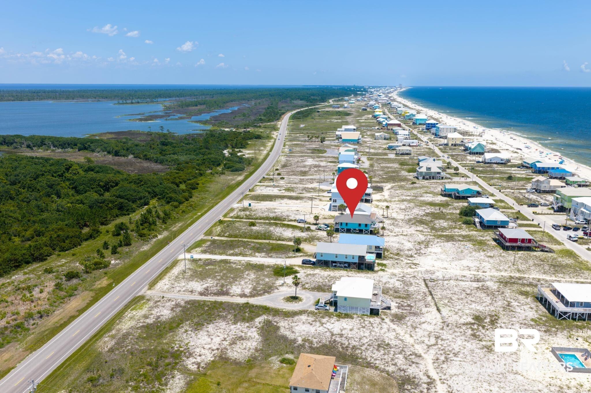Image 2: Coastal property featuring a long stretch of sandy beach and houses, with a body of water and lush green landscape opposite a two-lane road