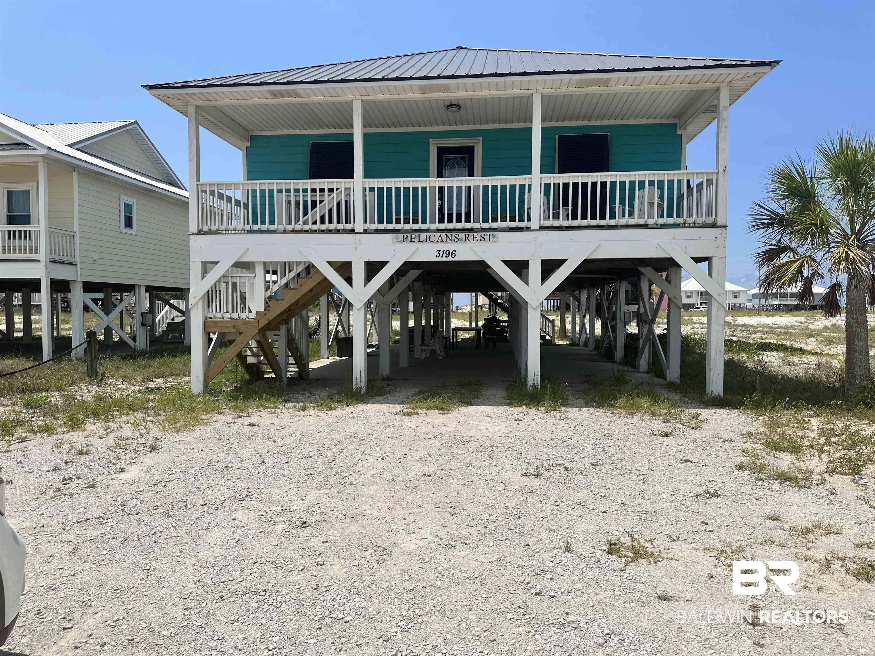 Image 3: Elevated coastal dwelling featuring a vibrant teal exterior, a covered front porch with white railing, and a durable metal roof