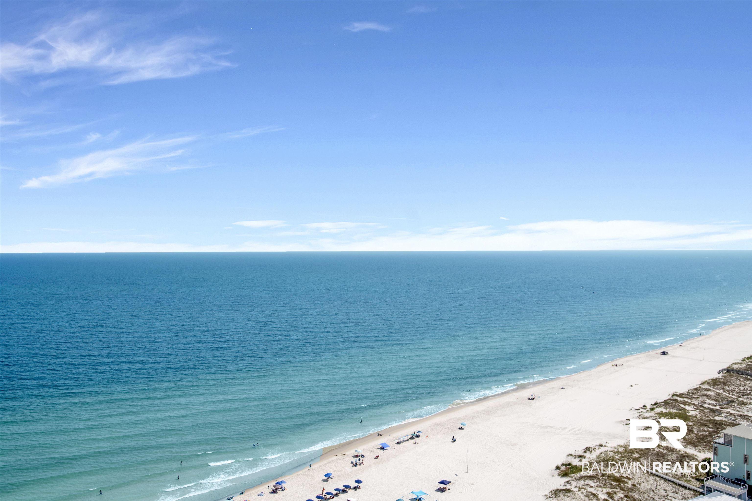 Image 4: Expansive coastal scenery featuring a wide sandy beach, turquoise ocean waters, and a clear horizon