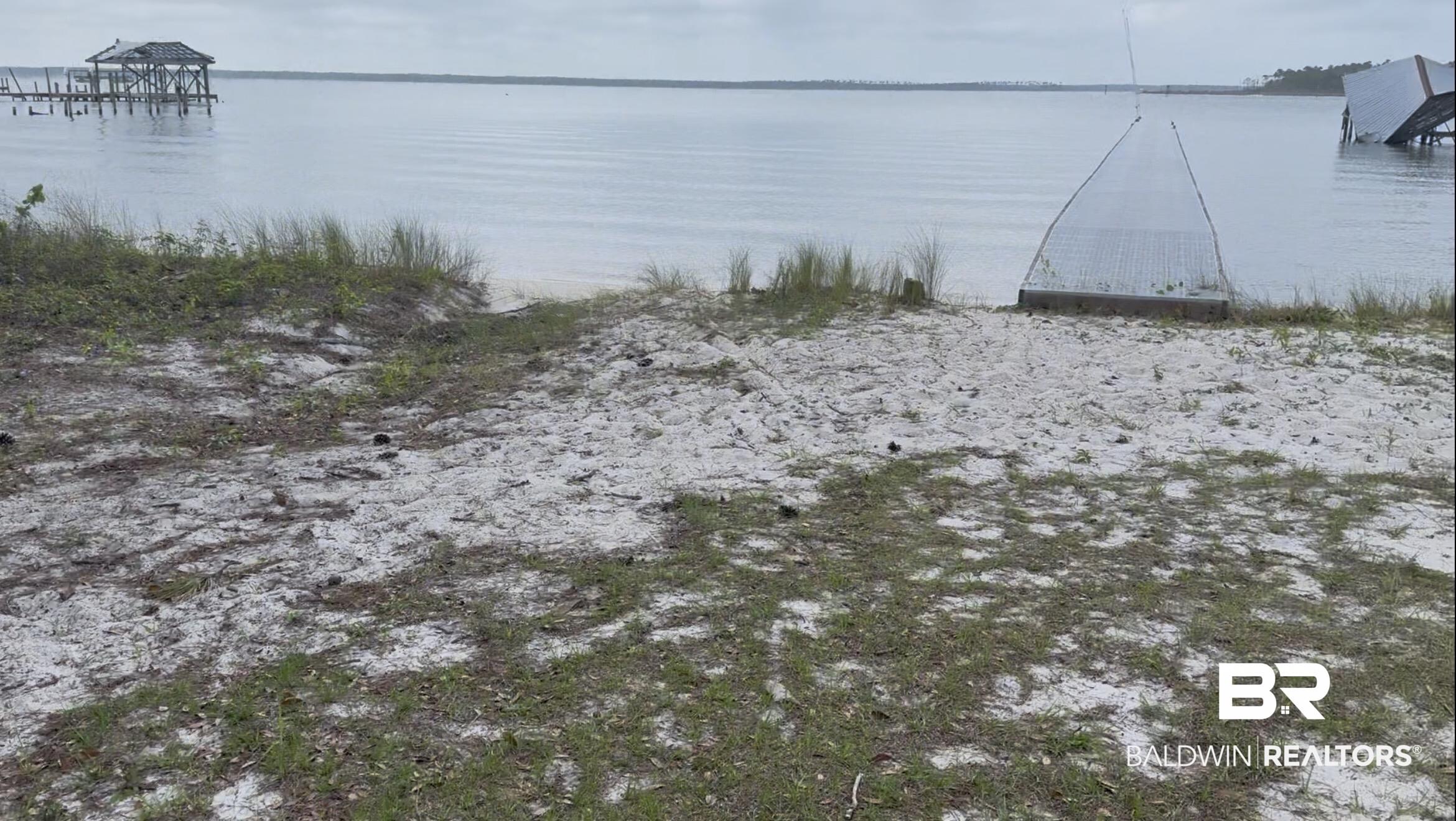 Image 4: Waterfront property featuring a sandy shoreline with natural vegetation and distant dock structures