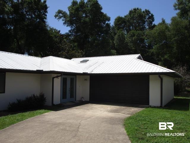 Image 2: View of front facade with french doors, driveway, a garage, stucco siding, and a metal roof