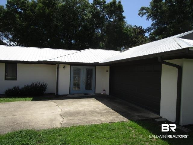 Image 4: Entrance to property featuring french doors, stucco siding, an attached garage, a metal roof, and concrete driveway