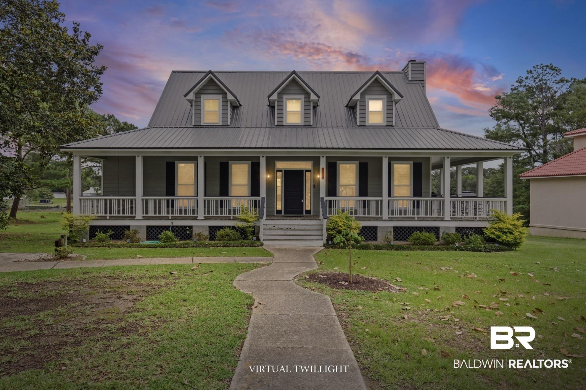 Image 2: Gray siding residence featuring a corrugated metal roof with multiple dormers, a full-width front porch with white railings and columns, and a central entry with black shutters framing the windows