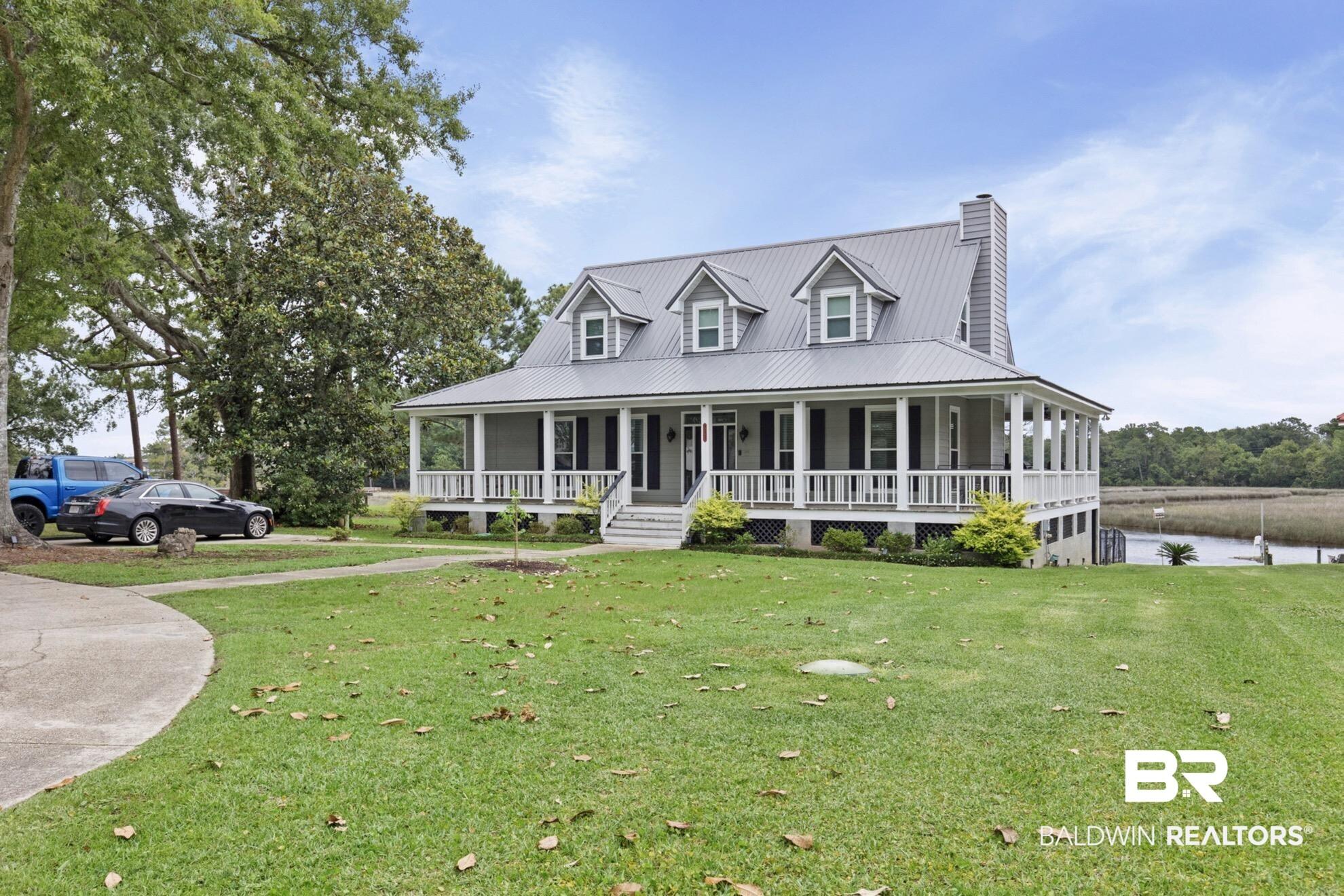 Image 3: Coastal residence featuring a metal roof, dormer windows, full-length front porch, white railings, and mature trees