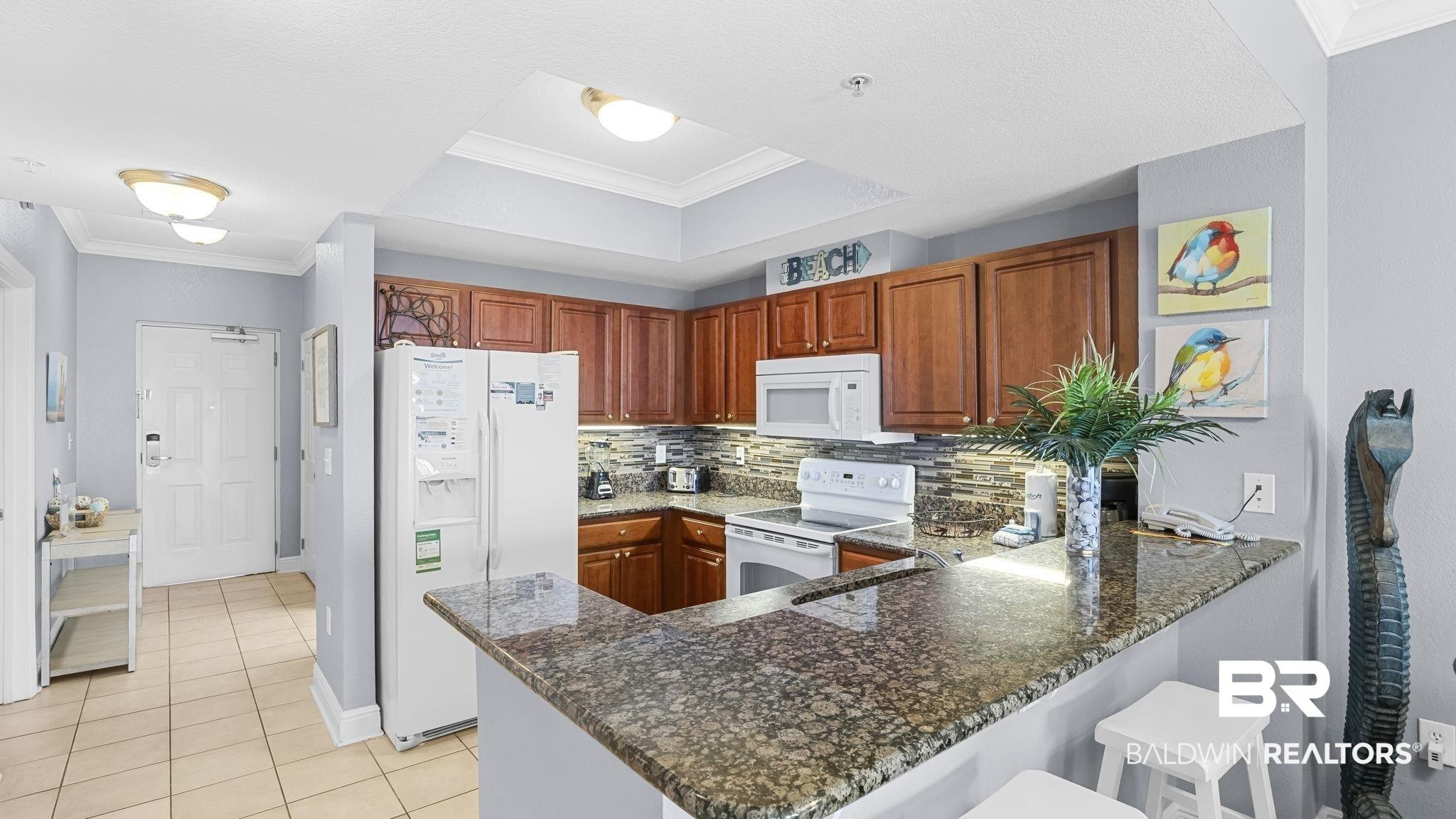 Image 3: Kitchen featuring a breakfast bar with stone-finish countertop, wood cabinetry, tile backsplash, and built-in appliances