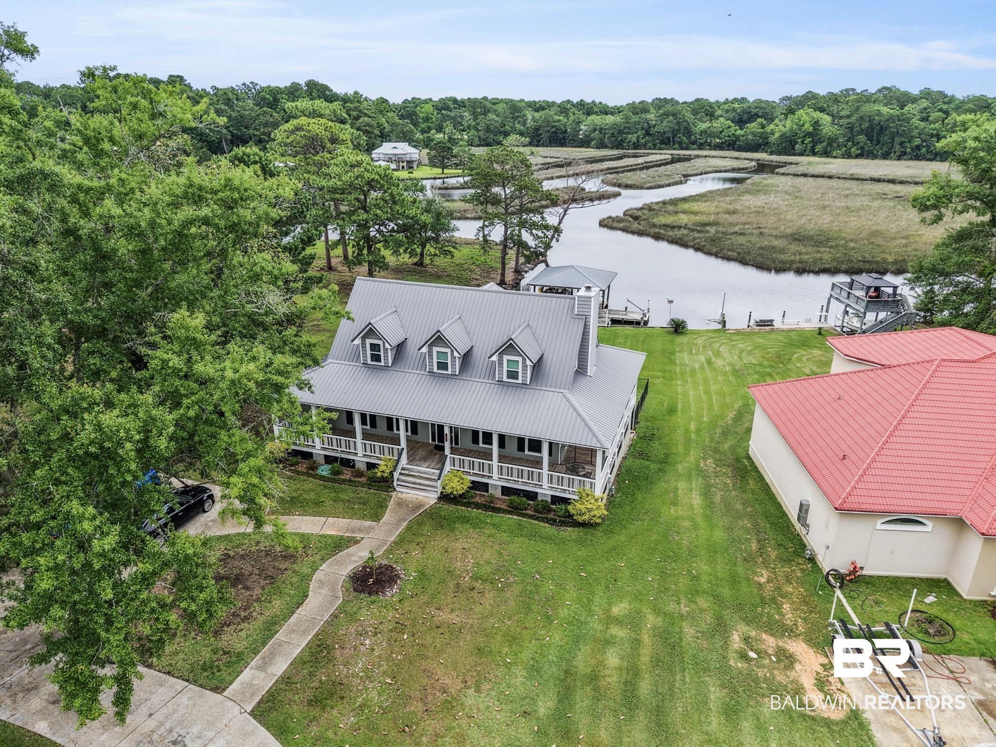 Image 4: Waterfront property featuring a main residence with an expansive covered porch, metal roof, and multiple dormer windows