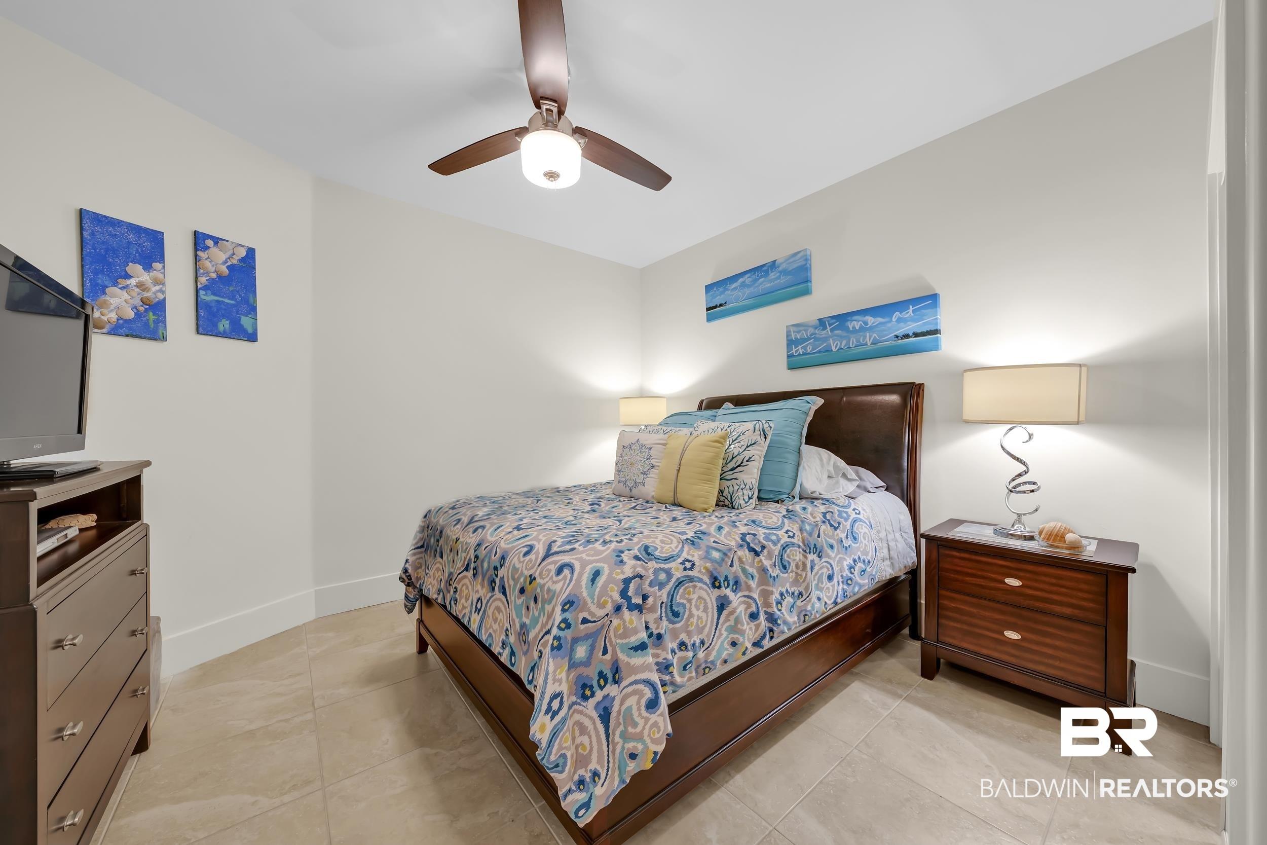 Image 4: Bedroom featuring neutral wall paint, tile flooring, a dark wood ceiling fan with integrated lighting, and white baseboards