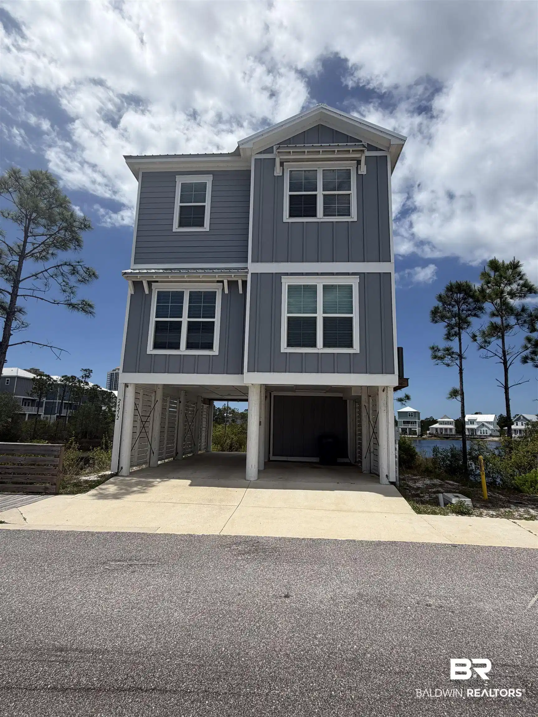Image 1: Three-story coastal residence featuring a light gray exterior with white trim