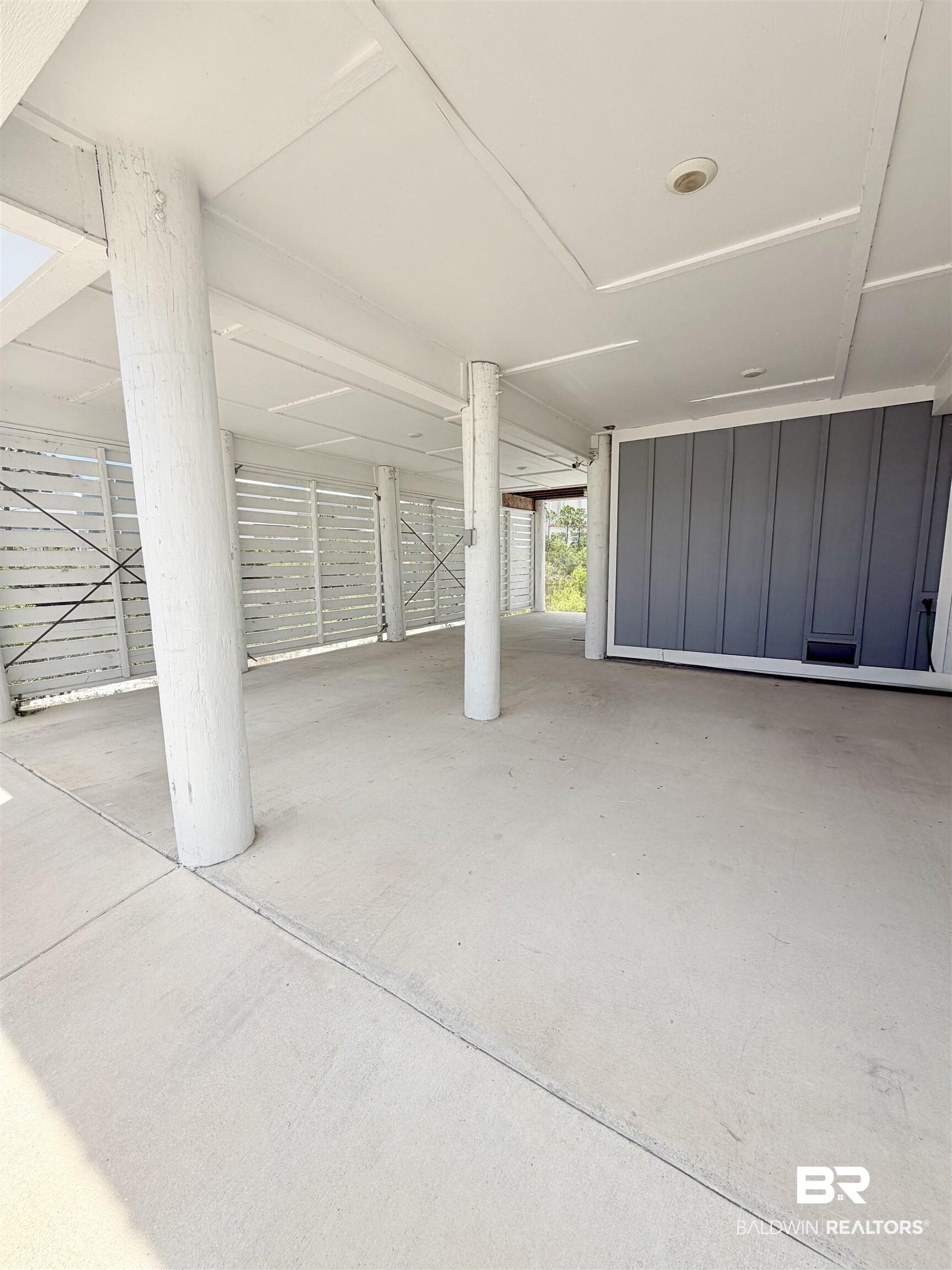 Image 4: Covered concrete parking area featuring structural columns, slatted privacy fencing, and recessed ceiling lighting