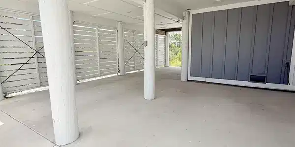 Image 4: Covered concrete parking area featuring structural columns, slatted privacy fencing, and recessed ceiling lighting