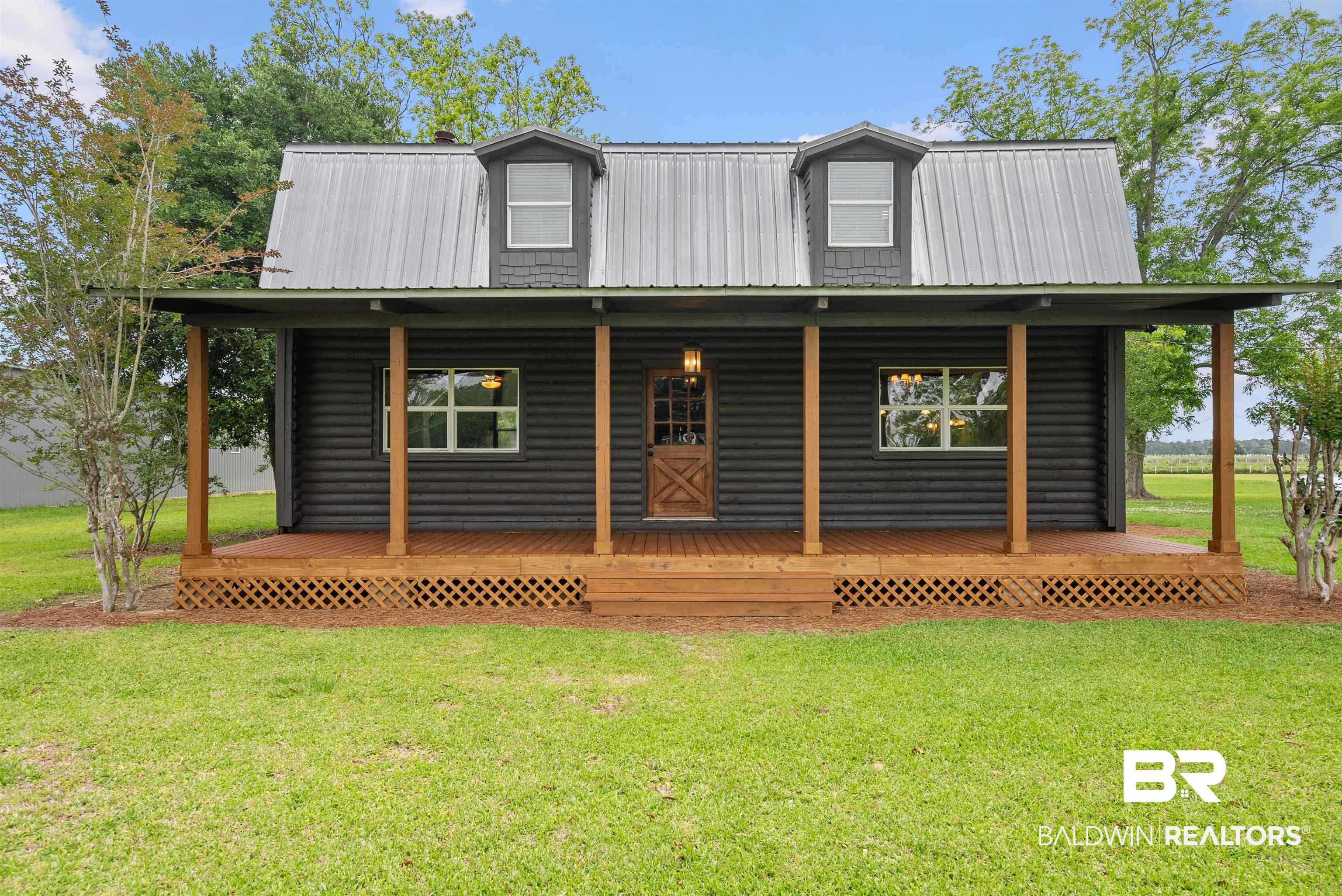 Image 2: Charming black log cabin exterior with a full-width covered porch, exposed wood support beams, and a metal roof