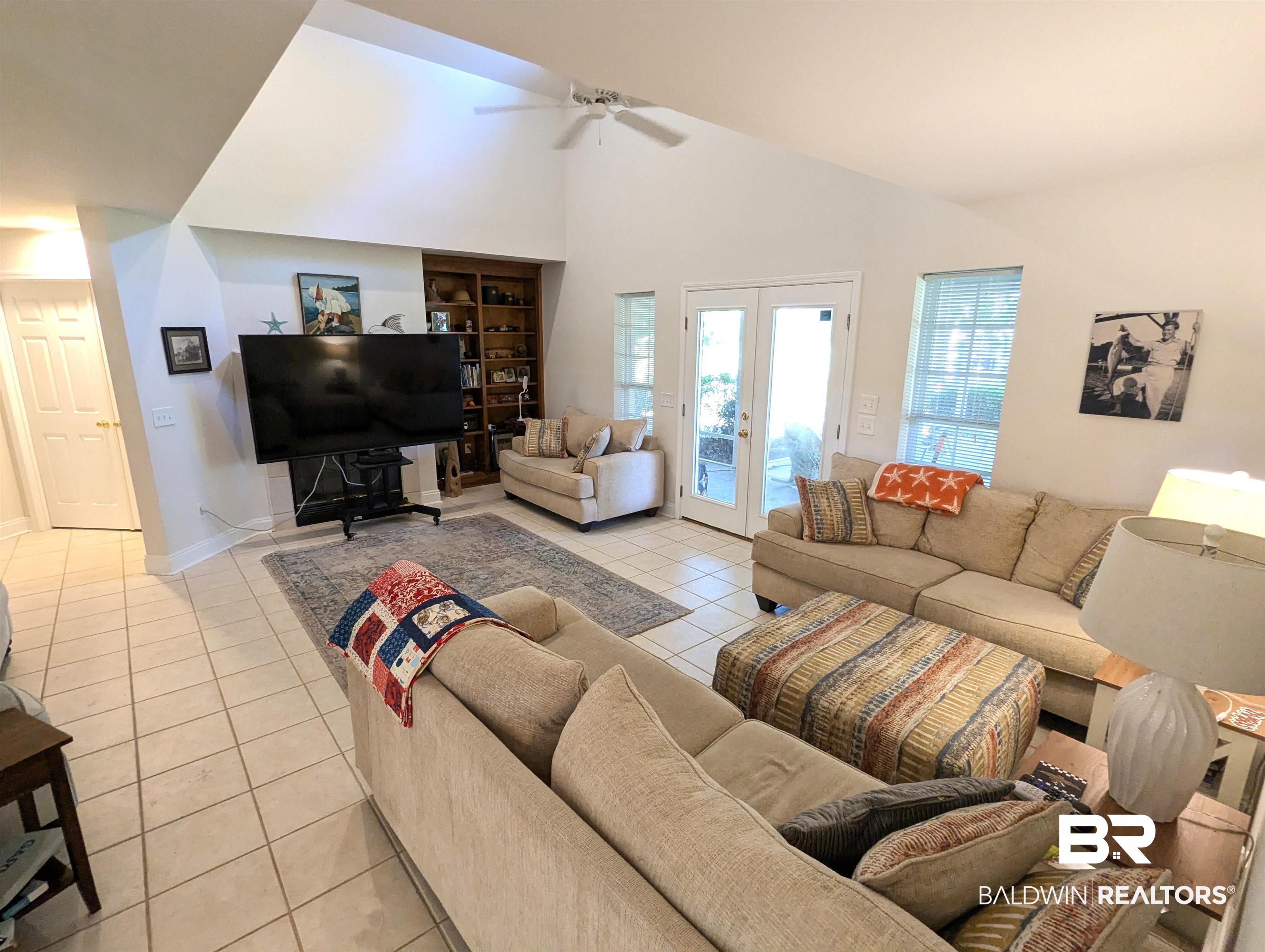 Image 2: Spacious living area featuring vaulted ceilings, tile flooring, built-in shelving, and exterior French doors
