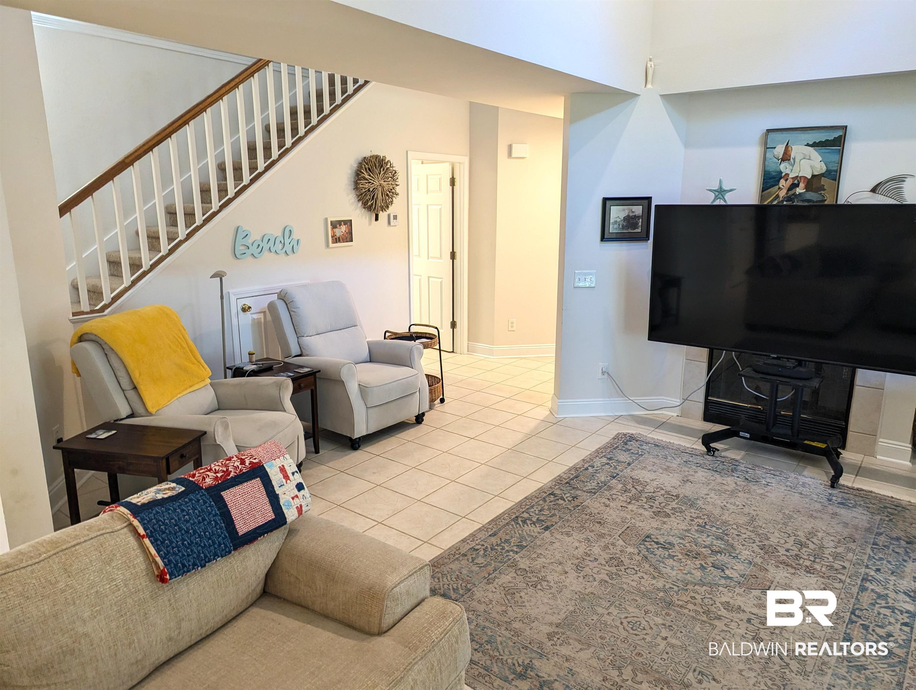 Image 4: Spacious interior featuring neutral wall tones, tile flooring, and a carpeted staircase with wood handrails