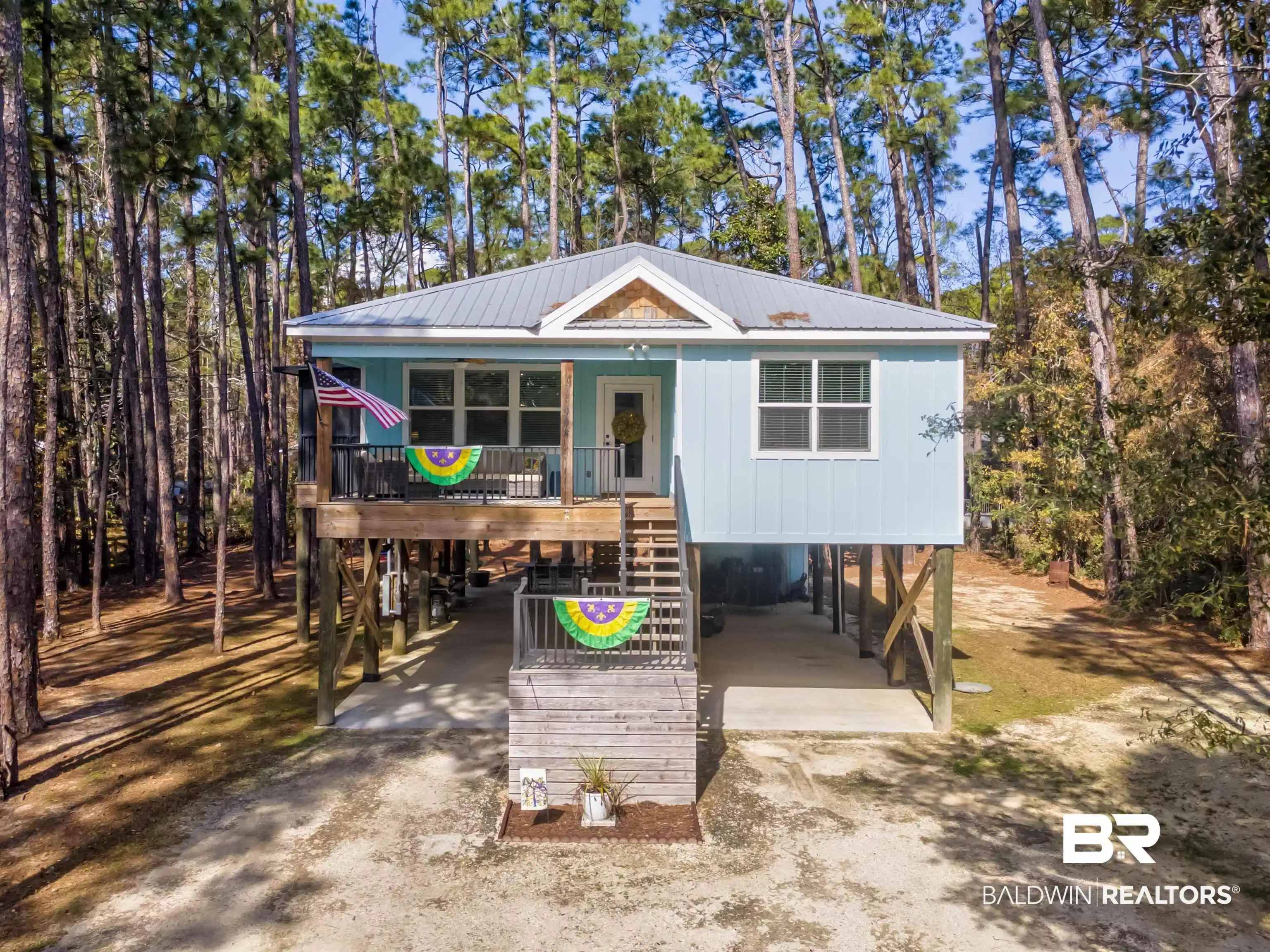 Image 1: Raised beach house with a carport, dirt driveway, a porch, and a metal roof
