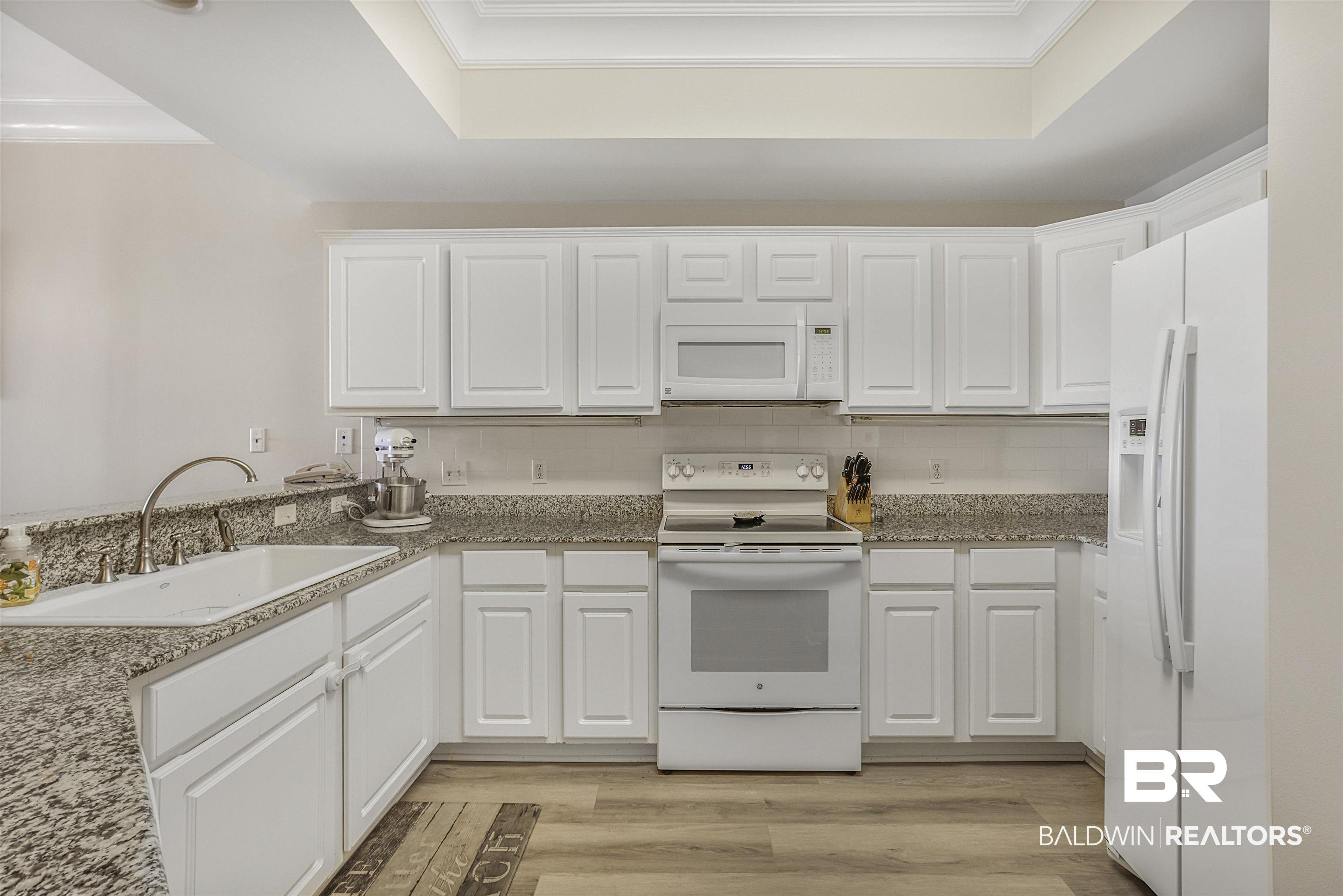 Image 3: Kitchen featuring white appliances, white cabinetry, light wood finished floors, decorative backsplash, and dark stone countertops