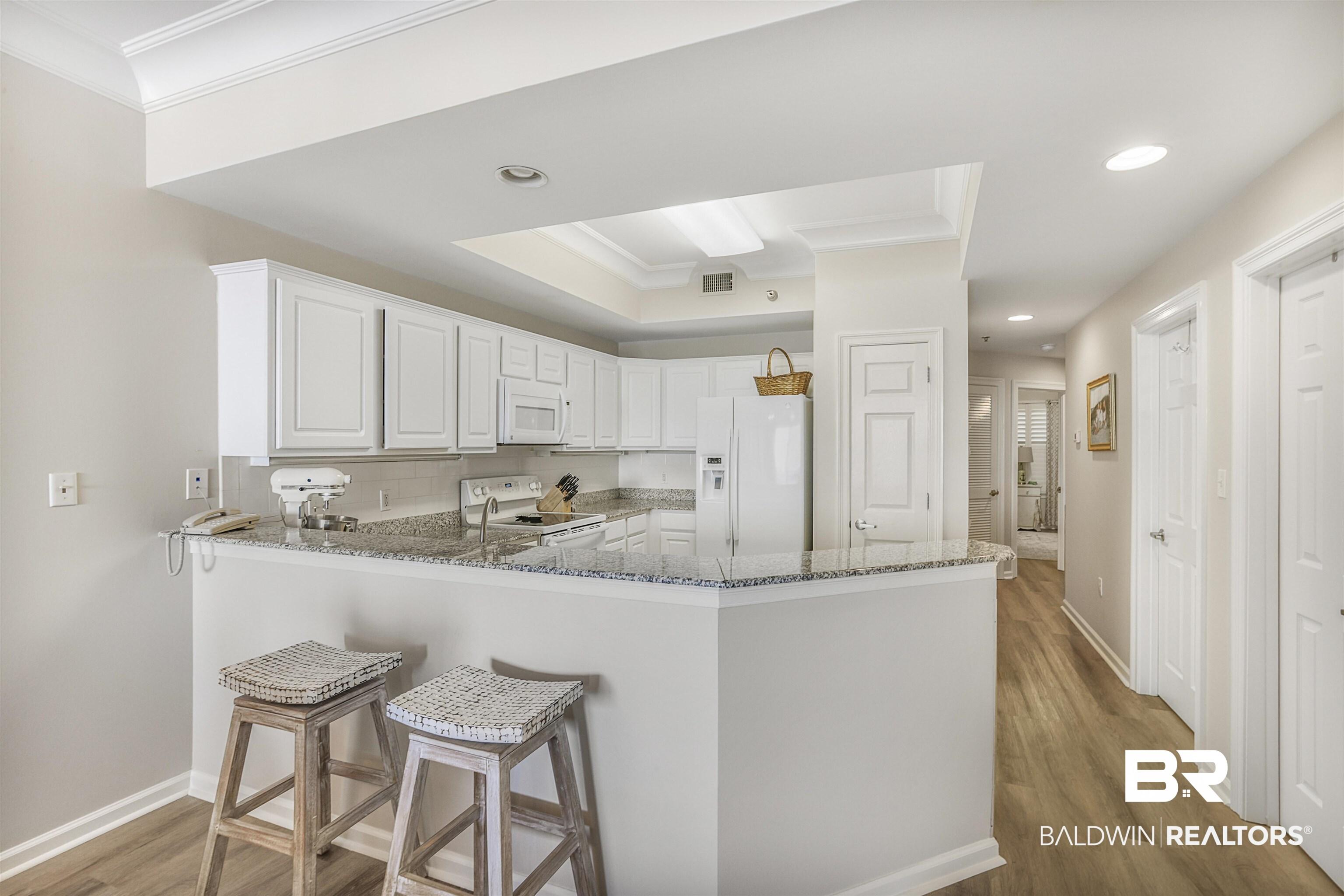 Image 4: Kitchen with white appliances, dark stone counters, white cabinetry, dark wood-style flooring, and ornamental molding