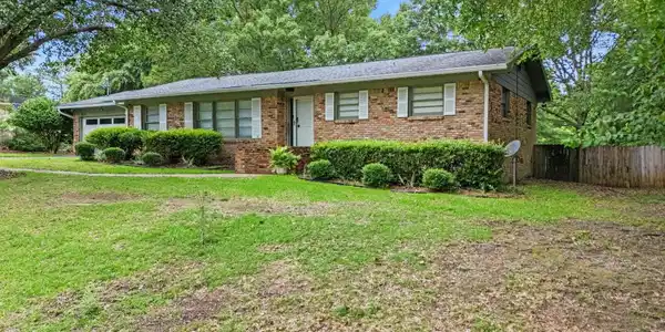 Image 2: Brick exterior residence with a single-car garage, white shutter accents, and established front landscaping