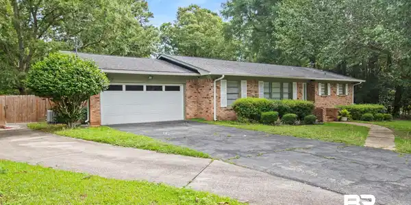 Image 3: Brick exterior residence featuring a two-car garage with transom windows, a concrete walkway, and established foundation plantings