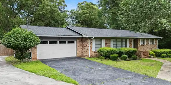 Image 4: Brick ranch-style residence featuring a dark shingle roof, white garage door, and white window shutters