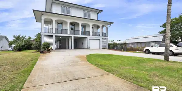 Image 2: Contemporary elevated residence featuring a large concrete driveway, integrated garage, and a covered ground-level parking area