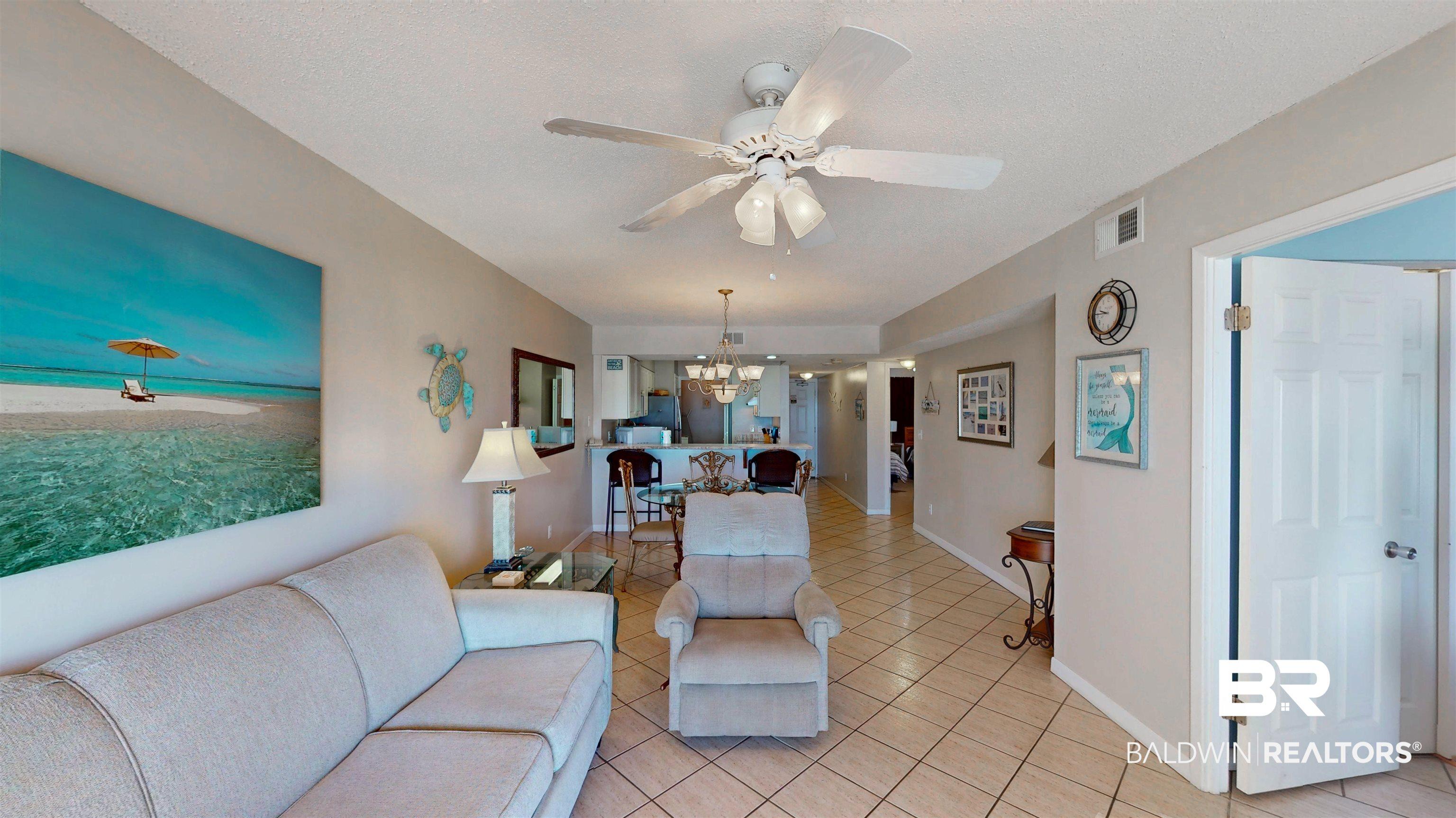 Image 4: Living area with light tile patterned floors, view of water and beach, a ceiling fan, a chandelier, and a textured ceiling