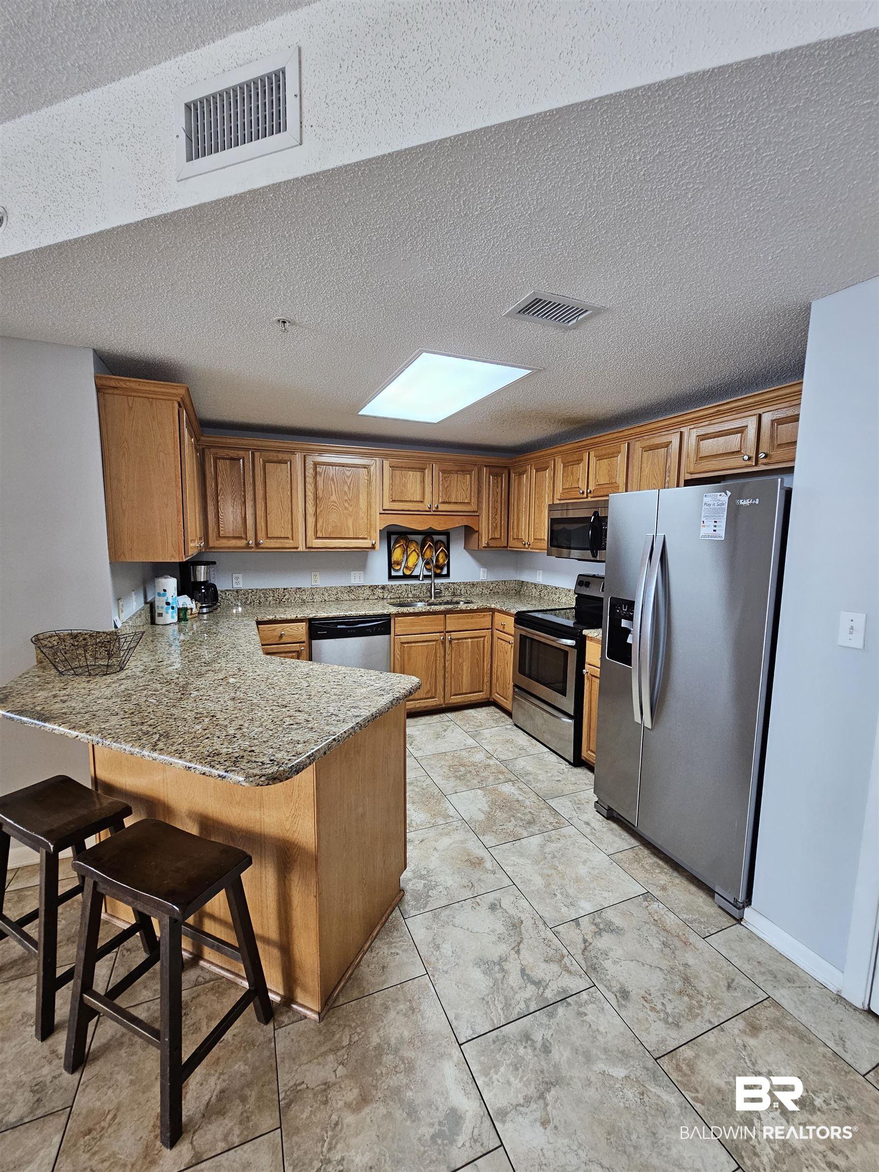 Image 3: Kitchen with stainless steel appliances, a peninsula, a breakfast bar, light stone countertops, and a textured ceiling