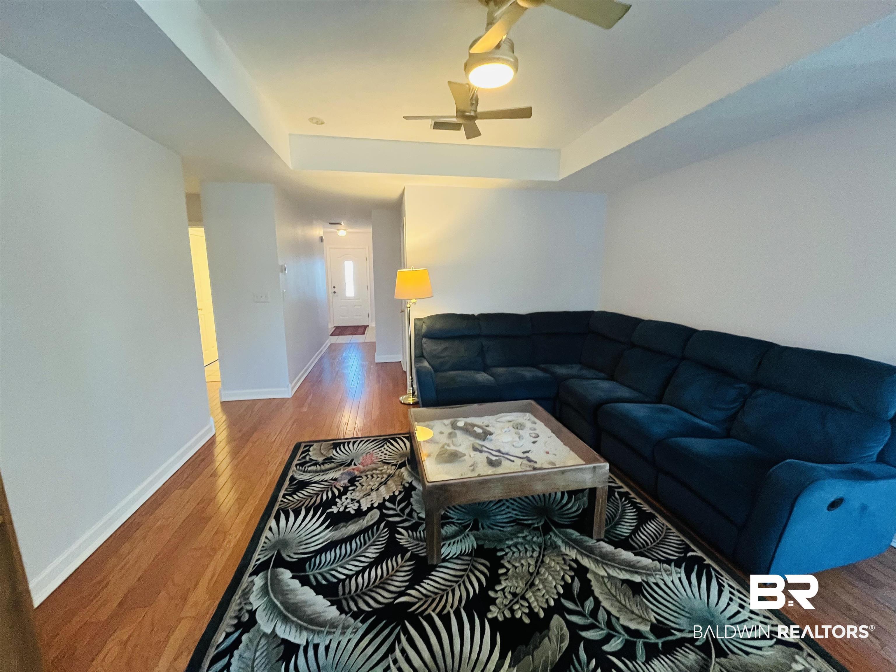Image 4: Living room featuring a tray ceiling, ceiling fan, and light wood-style floors