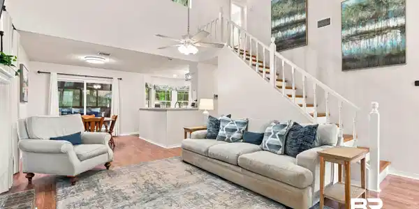 Image 3: Vaulted ceiling living room featuring wood-finish flooring, a white spindle staircase, and a ceiling fan with integrated lighting