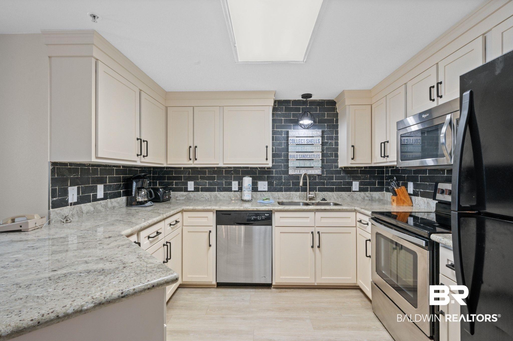 Image 3: Kitchen with sink, decorative backsplash, stainless steel appliances, and light stone countertops