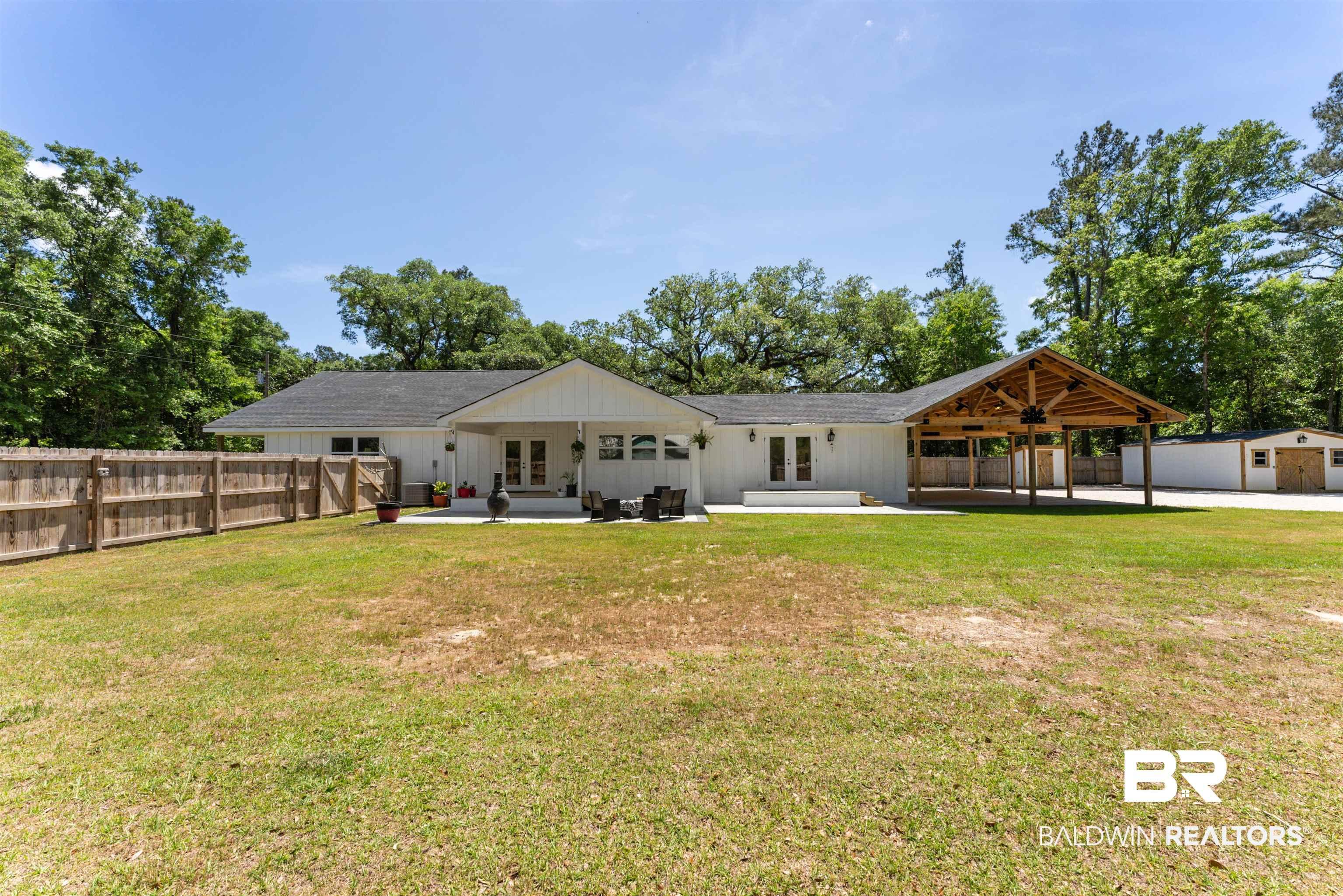 Image 1: Expansive backyard featuring a large concrete patio, a covered wooden deck with exposed beams, and a separate storage shed