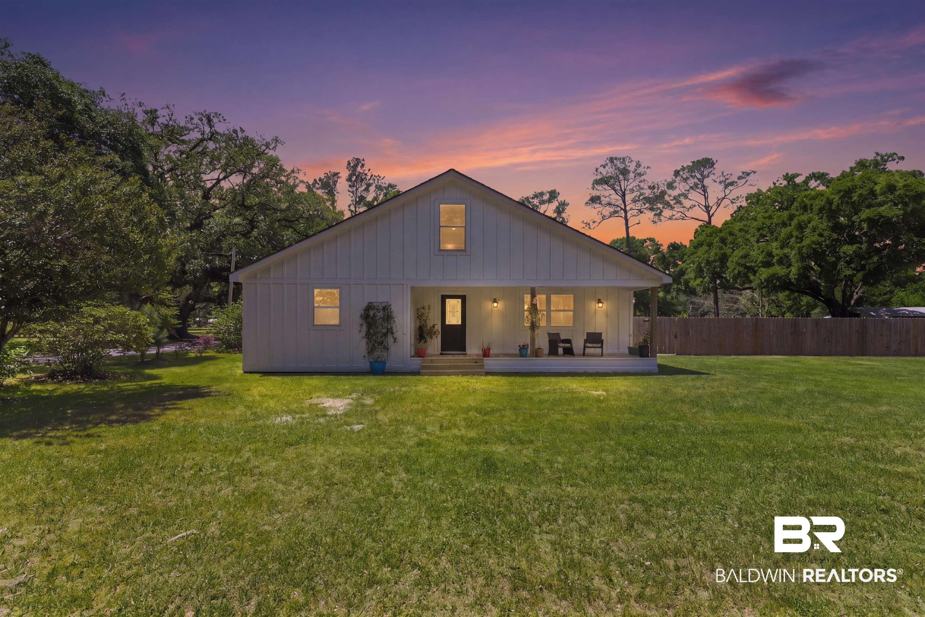 Image 4: Modern farmhouse exterior featuring board and batten siding, an inviting covered front porch, a dark entry door, and a spacious green lawn