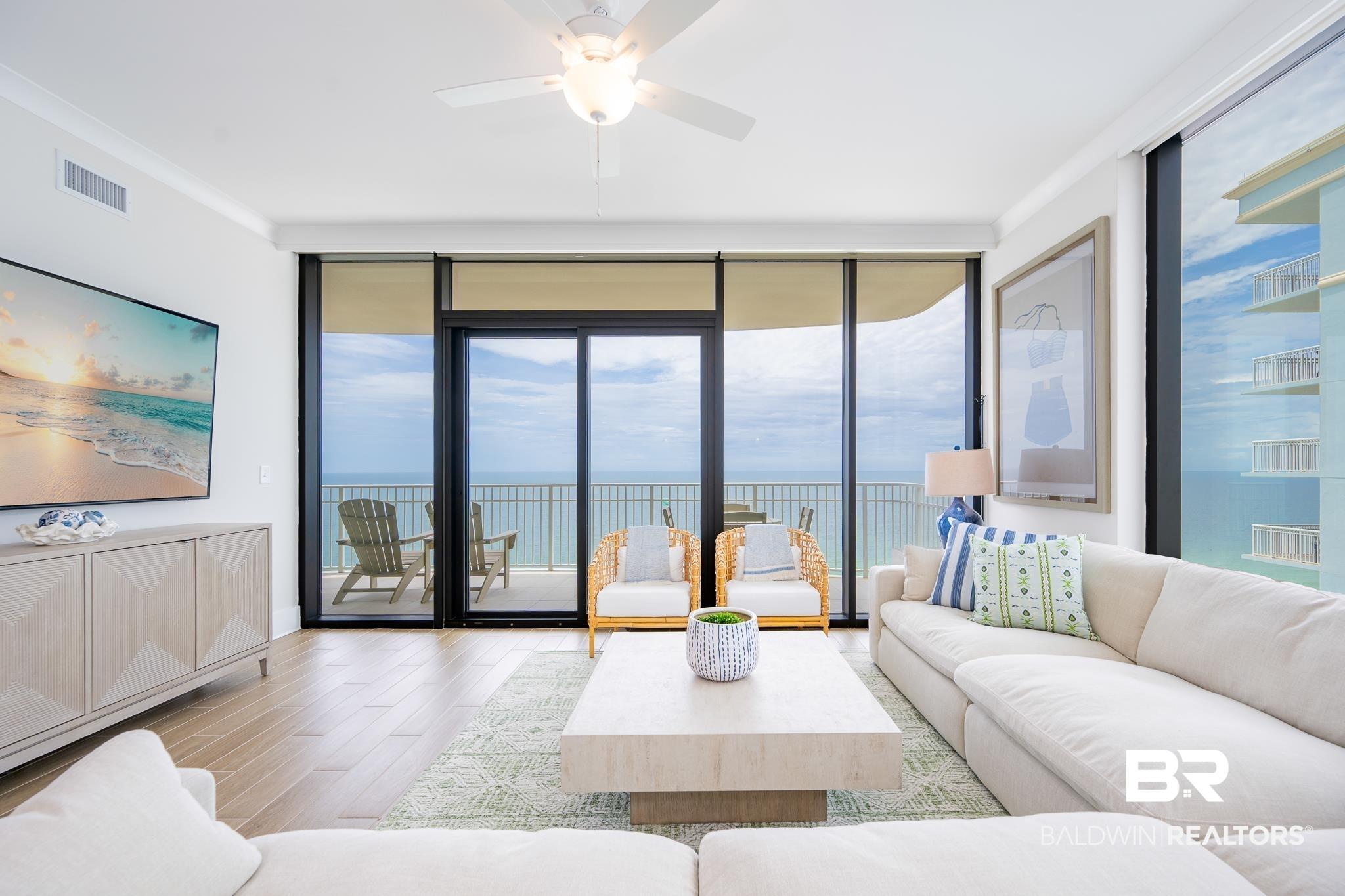 Image 2: Spacious living area featuring large sliding glass doors, wood-finish flooring, a contemporary ceiling fan, and access to an outdoor balcony