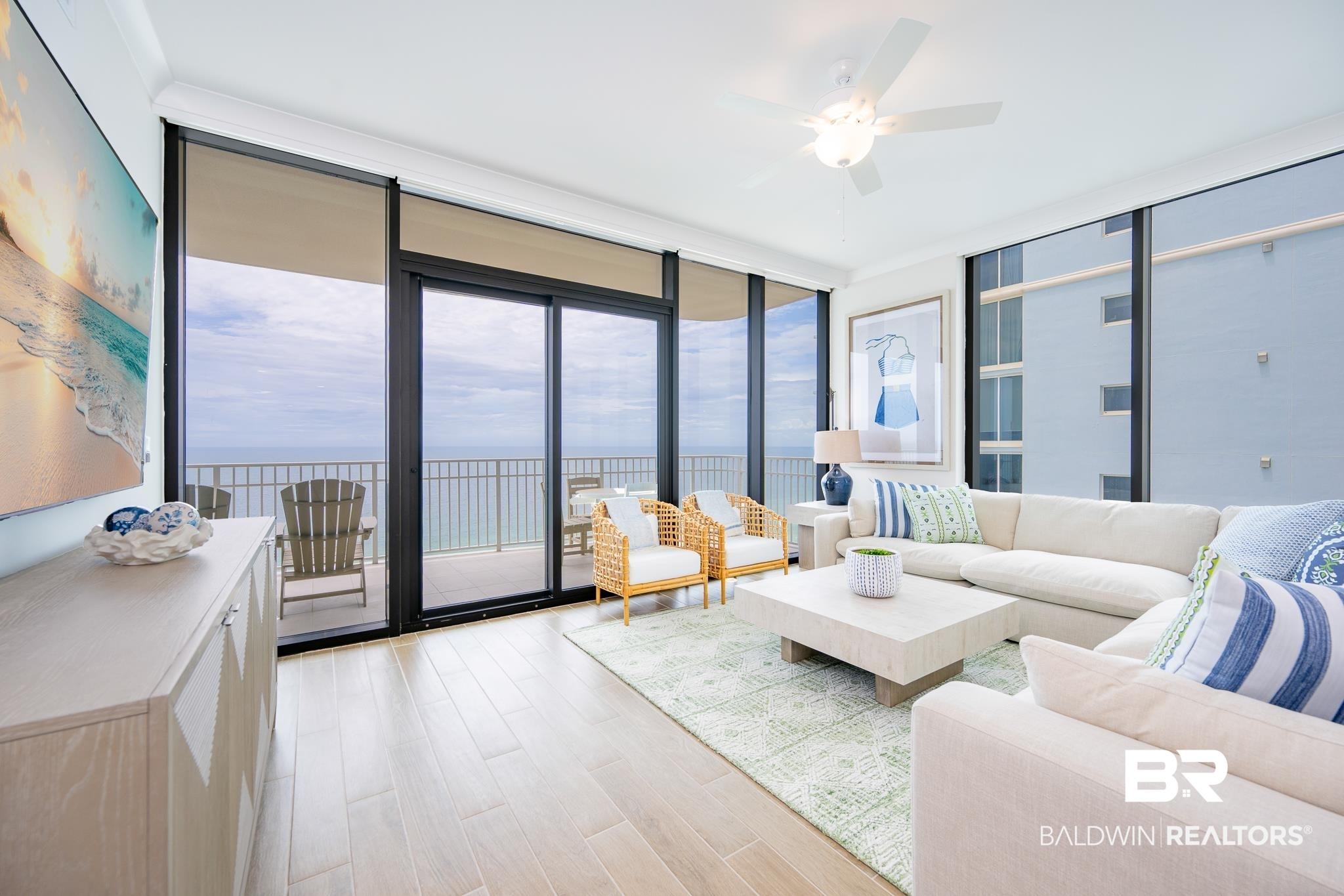 Image 4: Spacious living area featuring expansive floor-to-ceiling windows, light wood-finish flooring, a ceiling fan, and direct balcony access with metal railings
