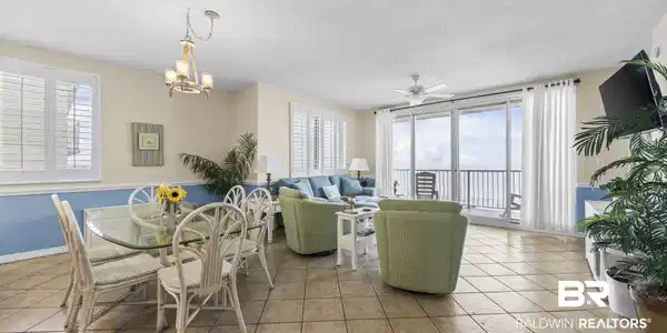 Image 4: Open-concept living area with tile flooring throughout, featuring a dining space with a chandelier and plantation shutters