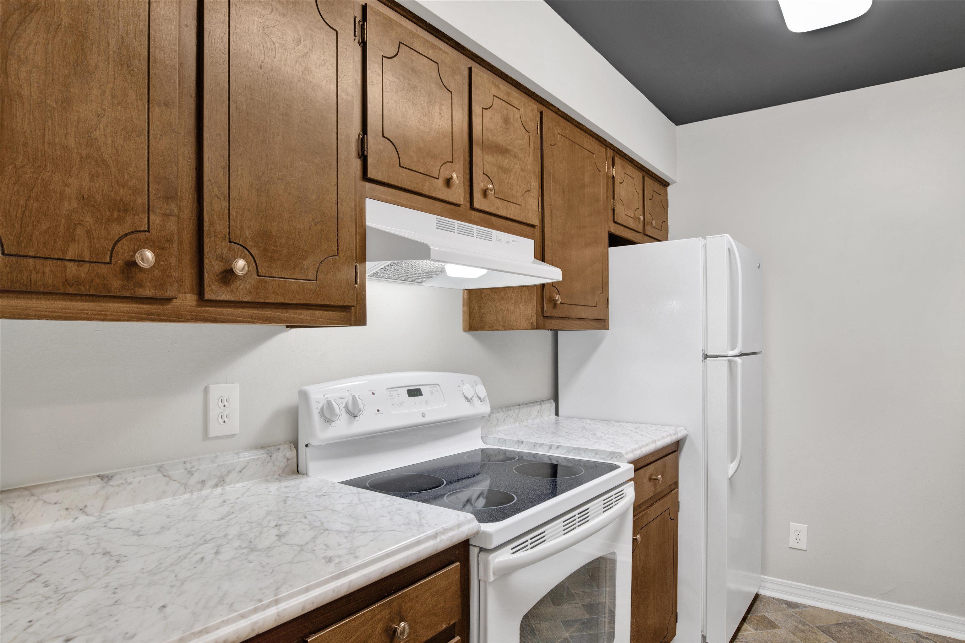 Image 2: Kitchen with white appliances, light countertops, under cabinet range hood, and brown cabinetry