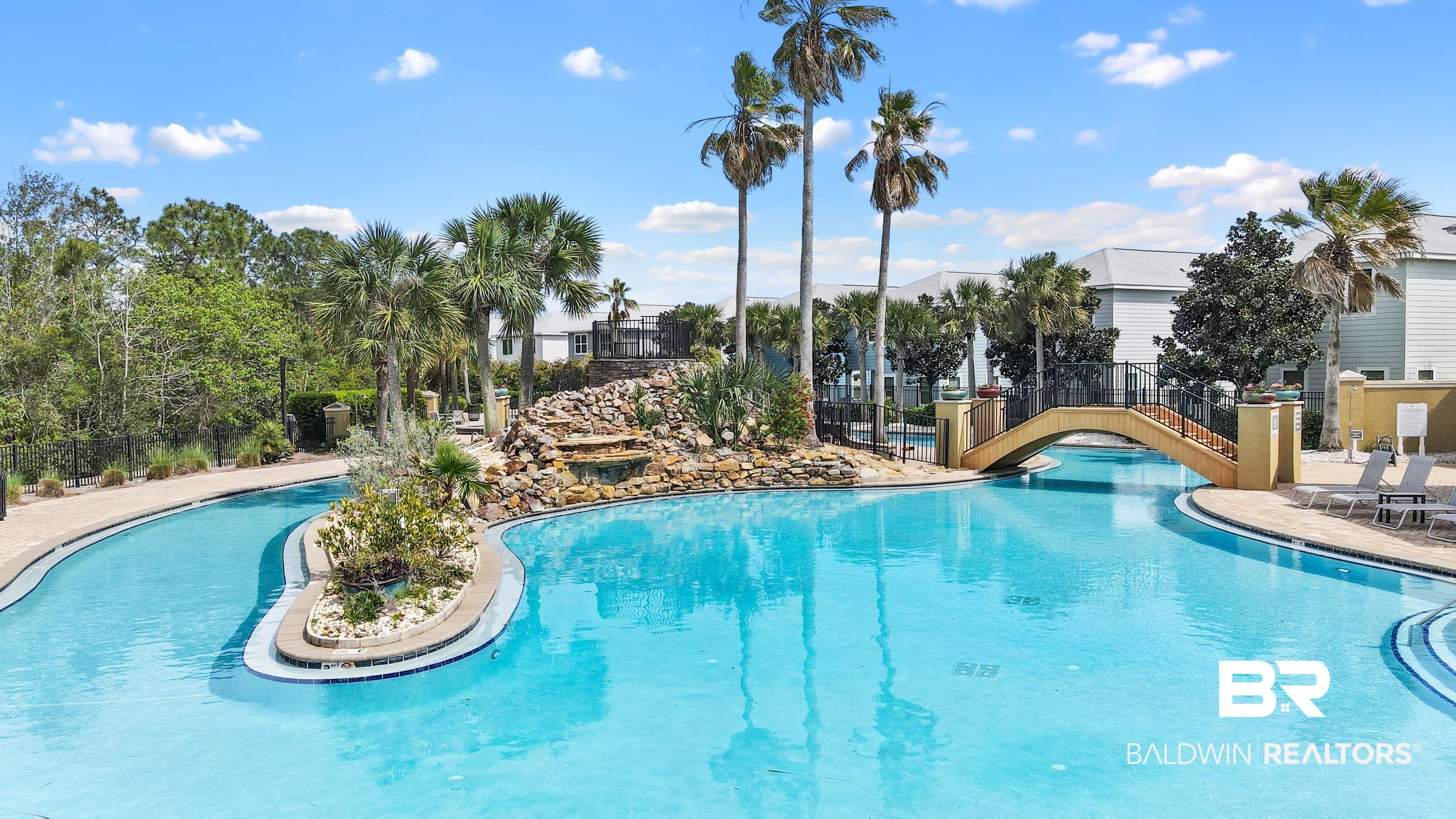 Image 2: Expansive resort-style swimming pool featuring a rock waterfall, a bridge arching over the water, a central landscaped island, and surrounding palm trees